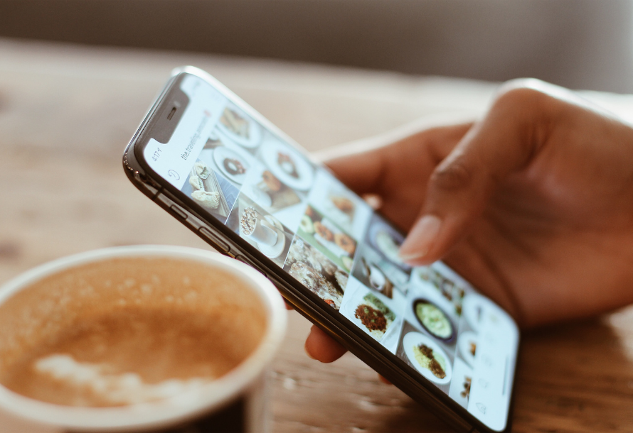 Person scrolling through Instagram with a cup of coffee on the table next to the phone.